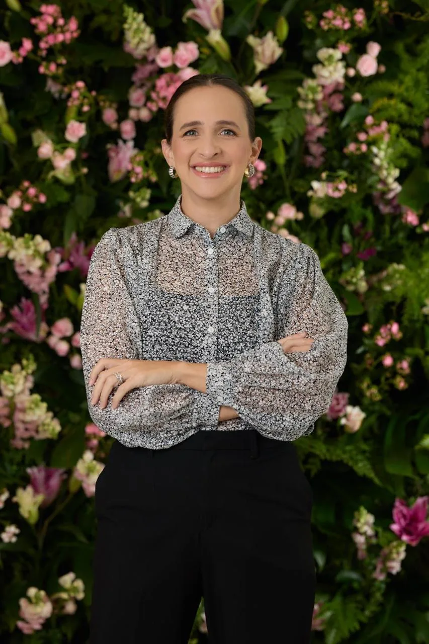 Tatiana Hara, fundadora da LURYA, sorrindo diante de um painel de flores